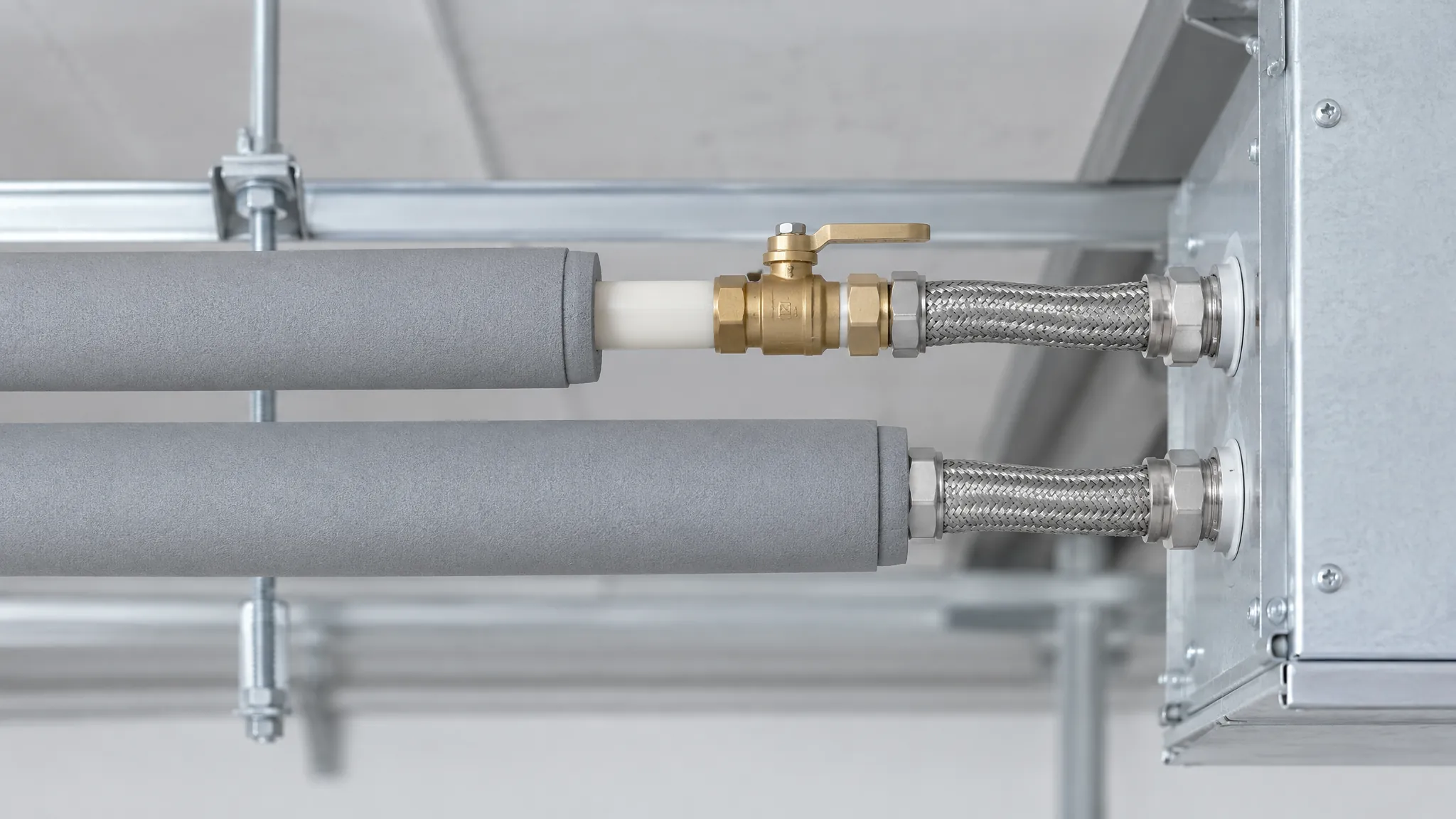 Insulated small-bore chilled water branch pipes running to a fan-coil unit, with a brass isolation valve on the short exposed section of pipe