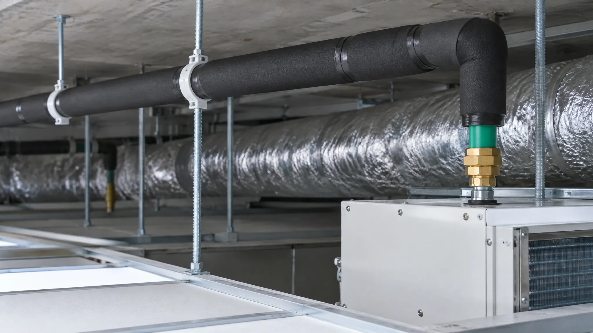 Insulated small-diameter plastic chilled water branch pipework in a ceiling void, dropping through a brass union into the casing of a concealed fan coil unit